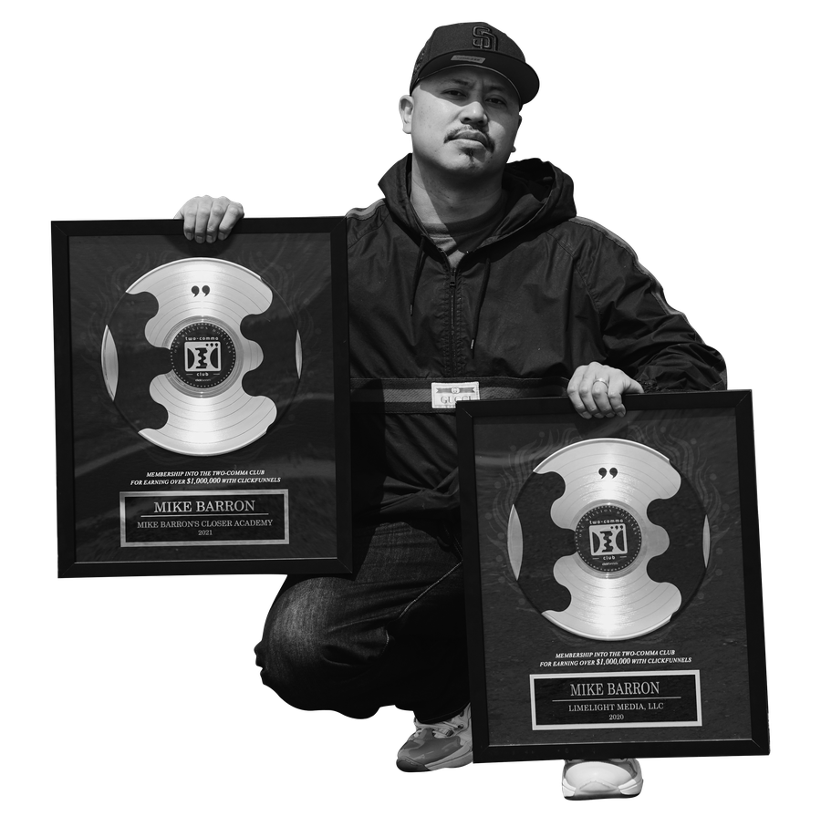 Mike Barron crouching in a black cap and jacket, holding two framed platinum record award plaques