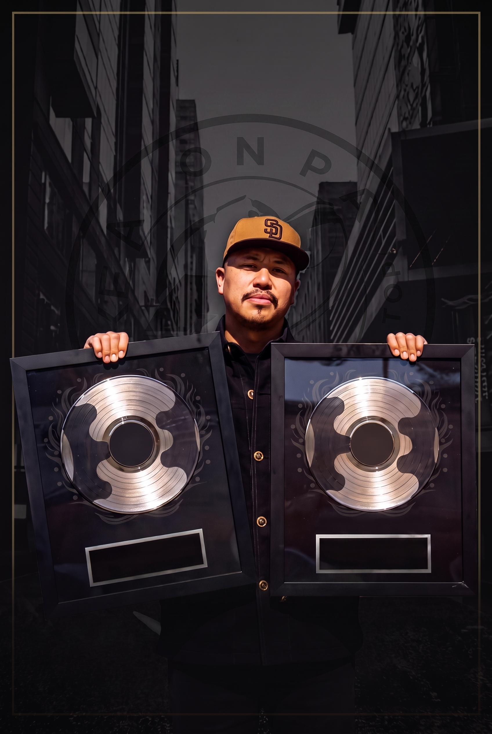 Mike Barron in a tan cap holding up two framed platinum record plaques in front of a black-and-white city street
